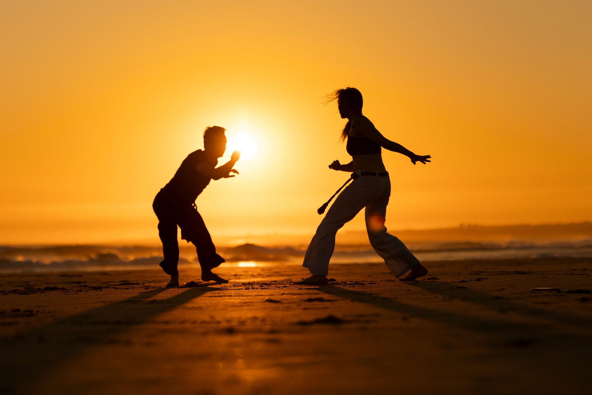 Two people are practicing martial arts on a beach at sunset