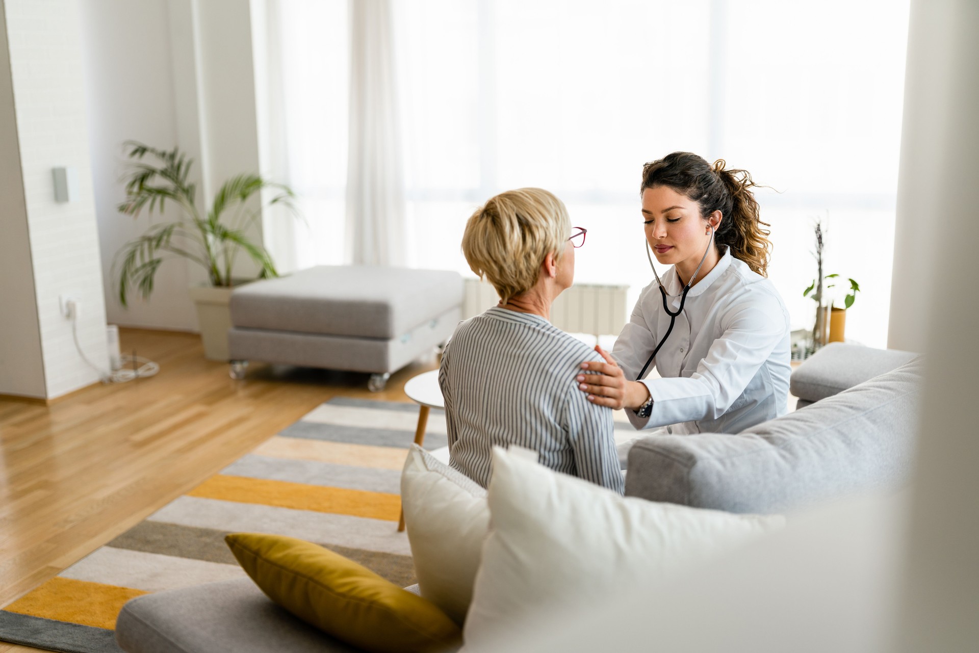 Attractive young female doctor checking senior patient with stethoscope